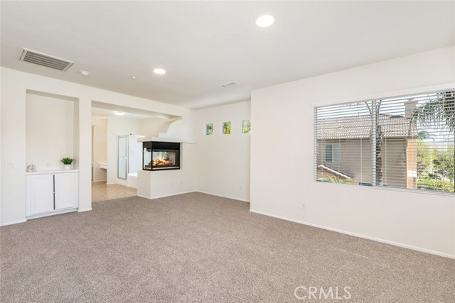 An expansive primary bedroom with a two-way fireplace, recessed lighting, and a picture window allowing tons of natural light