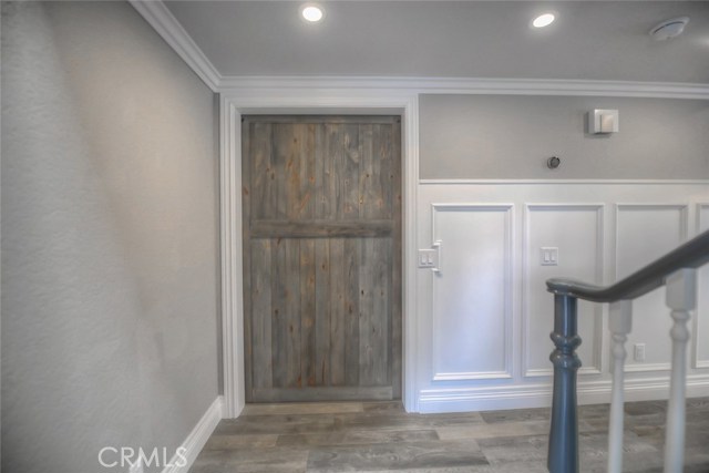 A look at the down stairs bedroom with the barn door closed - beautiful attention to detail blending the door, grey wood-like tile flooring, and raised panel wainscoting which is carried throughout the home.