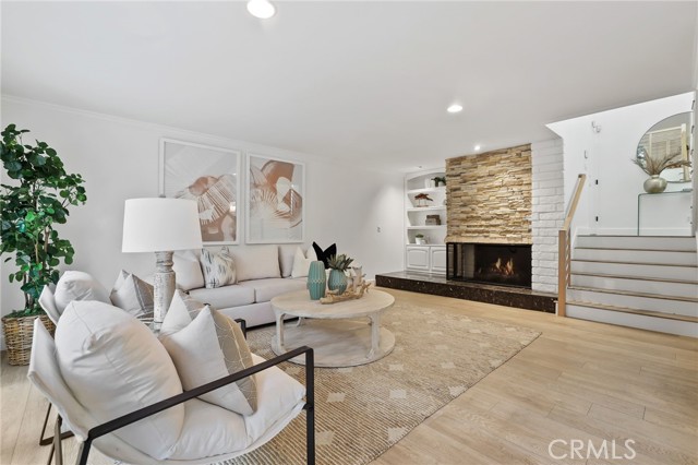 The expansive living room features a stone fireplace, complemented by built-ins, adjacent to a formal dining room – all seamlessly opening onto the wrap-around back patio, offering a side view of the Back Bay.