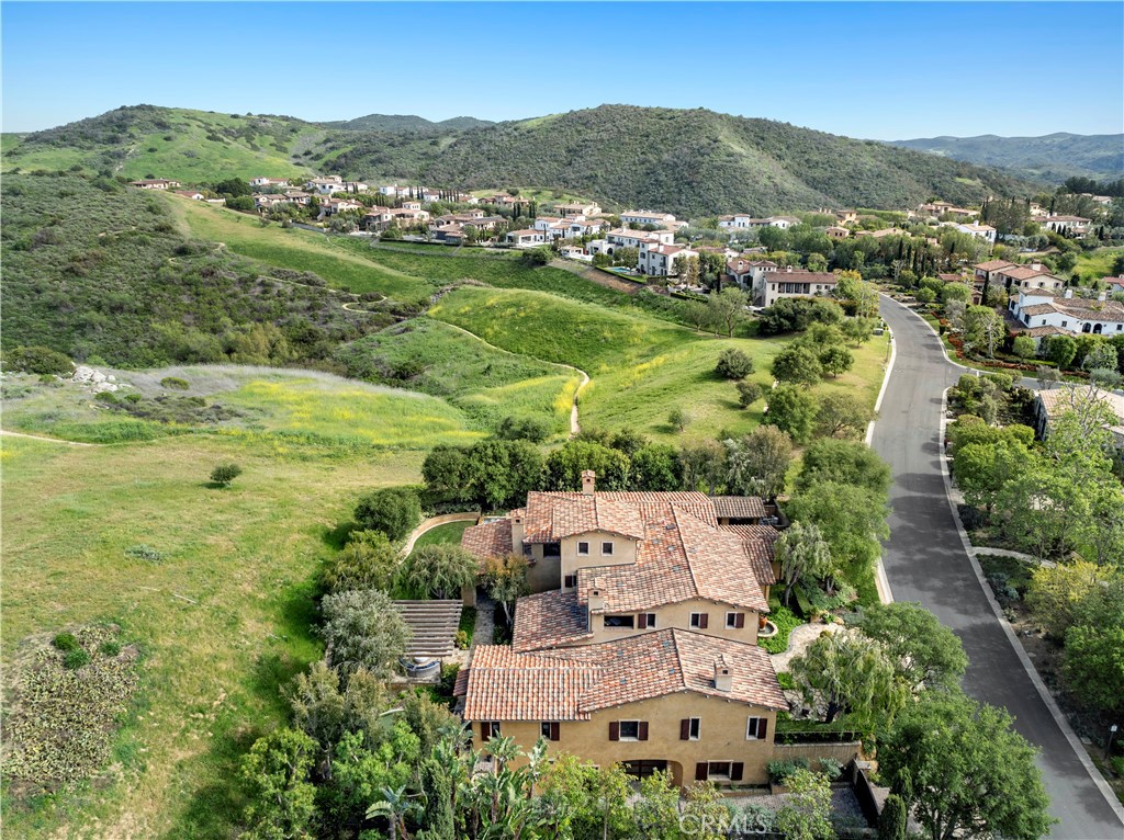 6 Bedrooms Including Two Primary Suites, 8-Car Garage, Elevator, Pool and More! This custom estate in the exclusive golf community of Shady Canyon presents a rare opportunity to own a private retreat in one of Orange County’s most prestigious enclaves. Set on a secluded lot with no neighbor to one side, this residence spans three levels and blends timeless architectural detail with refined modern living. A dramatic foyer with a barrel-vaulted ceiling welcomes you in and flows seamlessly into the elegant formal dining room, highlighted by wood coffered ceilings and expansive windows. Nearby, a formal sitting room with a cozy fireplace and a richly appointed executive office with custom built-ins offer intimate and functional spaces. The heart of the home is the chef’s kitchen featuring white marble countertops, soft-toned cabinetry, and a large center island. High-end appliances are integrated with ease, while a butler’s kitchen and vaulted wood-beamed ceiling add both charm and convenience. The sunlit breakfast room bridges the kitchen and family room, creating a comfortable space for everyday living and opening effortlessly to the poolside terrace. Designed for indoor-outdoor living, the backyard is a private sanctuary complete with a resort-style pool, BBQ pavilion, putting green, and manicured lawn-framed by lush landscaping and stone accents. The main level hosts a guest suite and junior primary suite. Upstairs, two additional bedroom suites and the grand primary suite await. The suite features a private kitchenette, stone fireplace, hardwood floors, and a wall of French doors that open to a large balcony with panoramic views of the hills, mountains, and city lights. The spa-like primary bath includes warm-toned marble, walk-in shower, oversized dressing room, and custom cabinetry. The lower level is an entertainer’s dream with a game room, full bar, gym with bath, and a home theater designed for a true cinematic experience. For car enthusiasts, the 8-car garage is a showpiece-complete with built-in cabinets and workspaces. Residents enjoy access to Shady Canyon’s world-class amenities: 24/7 guard-gated security, pool, tennis, pickleball, playgrounds, trails, and more.