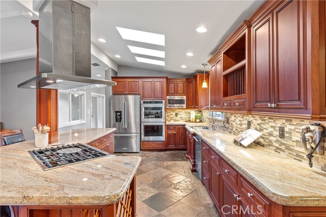 The entertainer's kitchen featuring stainless steel appliances, 6-burner cooktop with stainless steel hood, an ample amount of granite countertops for prepping and serving, gorgeous wood cabinetry with endless amounts of storage.