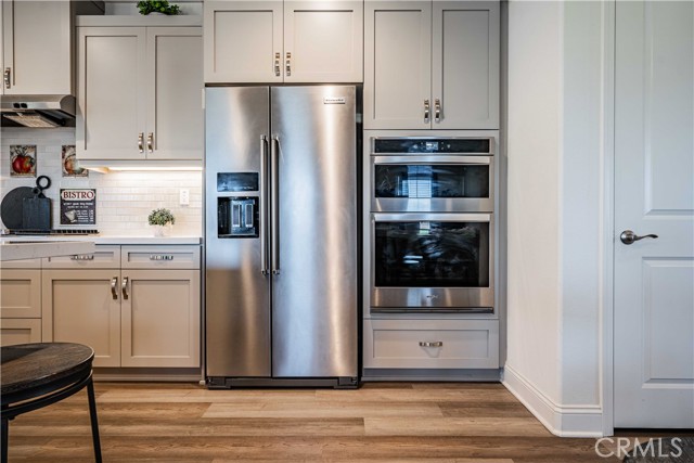 Stainless steel apliances here are the refrigerator, and double ovens. Top oven is a microwave and oven combo. Door to the right is a convienently placed closet that runs the entire length underneath the stairway. Soft close grey cuboards complimented by white quartz contertops, and white subway tile backsplash.