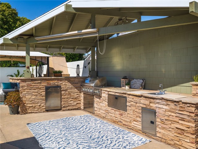 Covered BBQ area with grill, outdoor fridge & trash.