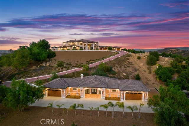 Welcome to Villa Dolce Vista. Commandingly positioned atop 20.39 ACRES at the north point of the EQUESTRIAN COMMUNITY of La Cresta, this Italian inspired masterpiece offers luxury amenities appreciated by the most discerning buyers. Impressive private GATED COMPOUND offers uninterrupted panoramic VIEWS of mountains, city lights, and the Temecula Valley. Encompassing nearly 14,000 SF, the resplendent home includes 5 EN-SUITE BEDROOMS, 8 BATHROOMS, a grand foyer with DUAL STAIRCASES and 24’ ceiling, elegant wood paneled STUDY, FORMAL DINING ROOM with fireplace and expansive city light view. Incredible CHEF’S KITCHEN includes a 20’ granite topped island, COPPER CEILING and LEDGER STONE WALLS. Extraordinary PRIMARY SUITE offers a FIREPLACE, BALCONY with staggering city light views, OPPULANT BATH with dual water closets, vanity areas, marble spa showers, and Jacuzzi tub. Massive GAME ROOM with full wet bar and access to the outdoor travertine deck with FOUNTAINS, INFINITY EDGE JEWEL SCAPE POOL AND SPA and two full outdoor BBQ kitchens. EIGHT CAR GARAGE with built in cabinetry. This SMART HOME is equipped with $155,000 in electronics that provides you with touch screen devices throughout the home. For extended family, a 1,977 SF SINGLE STORY 2 BEDROOM, 2 BATH BUNGALOW with two- 2 car attached garages. Energy efficient with a 47 KW 136 PANEL SOLAR SYSTEM powering both the main home and bungalow. 53’x40’ RV GARAGE totaling 2,120 SF for storage of two 45’ motorhomes plus all the toys. INCOME PRODUCING HAAS AVOCADO GROVE with automatic fertilization system and WELL watered with two 5000 gallon holding tanks. Additional building pad for future barn, tennis court or helipad. The La Cresta community is located mid-way between Orange County and San Diego County with convenient access to Ontario, San Diego, and John Wayne International Airport. This stunning estate is just minutes from the members only Bear Creek Golf Club offering a Jack Nicklaus designed golf course, tennis, and fine dining as well as the growing Temecula wine country.