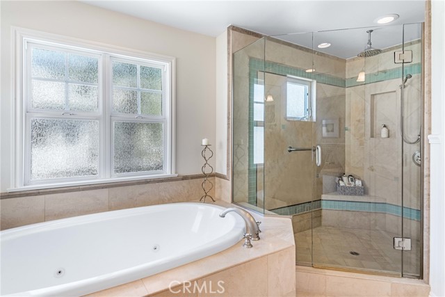 Primary bath with a beach inspired look featuring jacuzzi tub, frameless shower, his and her vanities