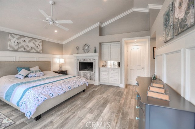 Master bedroom with built in storage, raised panel wainscoting, wood-like tile flooring, soaring ceiling, crown molding, and a spectacular fireplace.