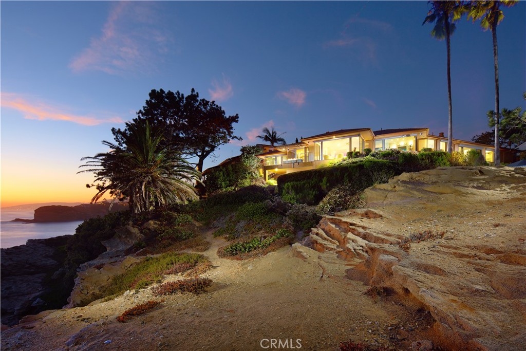 Rarely does a property of this magnitude present itself on the market. A custom ocean-view estate where artistry and nature unite on a blufftop promontory towering over the ocean. A welcoming home that is part luxury, part beauty, and 100% Laguna Beach. Enjoy views that encompass Dana Point, Catalina Island, colorful sunsets, breaking waves, and twinkling evening lights are viewed from most indoor and outdoor living areas at the estate. Located at the end of a private cul-de-sac in South Laguna’s gated Three Arch Bay, the appx. 2.15-acre property encompasses the bluff and part of the beach below. Custom hand-carved mahogany garage doors and a matching entry gate enrich curb appeal, and a private courtyard with Inca Gold natural stone welcomes all with a pool with water feature, electric cover and massaging jets; a built-in  Twin Eagles BBQ bar and Salamangrill and retractable Sunbrella awning; two fire pits and outdoor shower; a full outdoor bath; Bromic heater; and bespoke art from Laguna’s renowned Marlo Bartels. Floor-to-ceiling windows, glass doors, and sliders from Germany’s NanaWall unite exterior spaces with a fabulous interior, where immediate ocean views are experienced upon entry. Main living areas comprise a custom walk-in wet bar with ice-effect glasswork, handmade African movingui cabinetry, a see-through fireplace, a grand dining room that opens to the pool, and a family room with access to an outdoor view deck. The kitchen is as beautiful as it is functional thanks to an island with Brazilian granite top, custom aluminum-finished cabinetry crafted by Bulthaup in Germany, two built-in Miele refrigerators, and a suite of Gaggenau appliances. Blue Bahia and Blue Pearl Granite shine in the primary suite, and select secondary baths reveal Keuco vanities and mirrors. The lower-level theater is accessed by a Garaventa lift and features state-of-the-art A/V equipment. A garage with lift accommodates four cars, a driveway that can fit up three cars, and a Kohler gas backup generator, Lutron lighting, Elan audio, an aluminum roof by Future Roof Systems of Canada, fast water-heating systems, and a 500-gallon whole-home reverse-osmosis system are included.