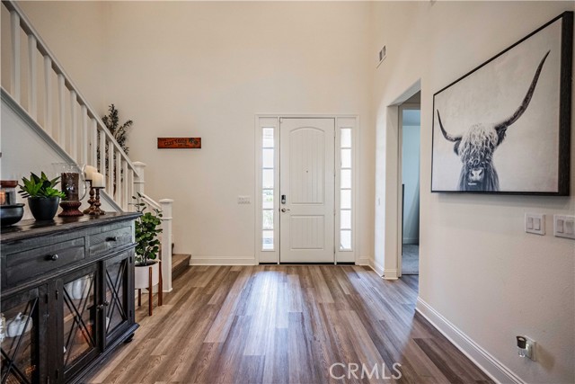 Front entry is grand with soaring ceilings, recessed lighting, stunning grey/taupe wood laminate flooring. White walls and baseboards with white trimmed stairway. First door to the right is the downstairs bedroom and full bath, nicely tucked behind the wall.