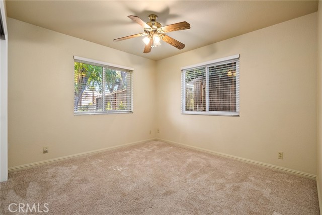 Bedroom has plush carpet, ceiling fan and large windows.