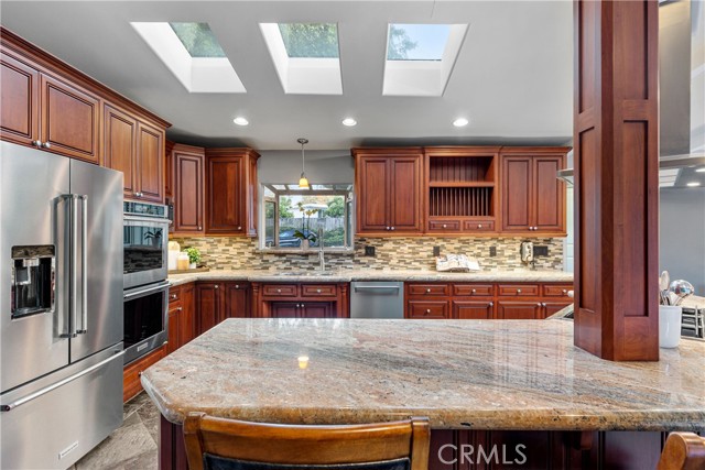 The entertainer's kitchen featuring stainless steel appliances, 6-burner cooktop with stainless steel hood, an ample amount of granite countertops for prepping and serving, gorgeous wood cabinetry with endless amounts of storage.