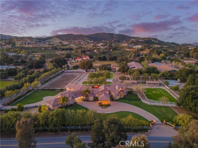 Welcome to the epitome of luxury living in the prestigious La Cresta Estates. This stunning gated estate sprawls over 5 acres, offering an unparalleled blend of luxury and tranquility with over 8,500 square feet of living space. An impressive motor-court and covered loggia welcome you into a world of refined living. Upon entry, the formal living area captivates with a stately fireplace, soaring ceilings, and French doors that open to the expansive outdoor yard, pool, and entertaining area. A gourmet kitchen is complemented by light and bright windows and a large walk-in pantry equipped with additional refrigeration. The formal dining area serves as a natural extension of the living space and provides a perfect setting for intimate dinners or formal festive gatherings. The main level also offers two offices and a large bonus room complete with cinematic entertainment, indoor activity space, and a full bar. Each bedroom suite is a spacious retreat with a convenient bedroom on the main level. The primary suite is a sanctuary of indulgence, featuring a wet bar, two sets of sliding glass doors, and panoramic views of the estate and hills. The primary bathroom has an oversized soaking tub, dual sinks, vanity, heated stone floor, two walk-in closets, and a steam room option in the shower. The property's outdoor oasis is a haven of leisure, featuring a pool, spa, and a sprawling area for al fresco entertaining. The estate lends itself to those with equestrian interests, offering an ideal equestrian property and training facility. Amenities include an 8-stall breezeway barn with indoor/outdoor box stalls,  a 4-stall "horse motel" with indoor/outdoor stalls, and a large roll-up garage perfect for horse trailers or storage. Additionally, there is a tack room, washroom, feed room, and laundry room. The covered Olympic-level training arena is equipped with mirrors and premiere arena footing, and there is an outdoor training arena as well. The property features 3 grass pastures and 2 dirt turnouts, providing ample space for horses to roam. The estate also includes a massive workout room with full-length mirrors and a ballet barre, a 4-car garage attached to the house, a built-in gas generator, and a property with its own water well system.