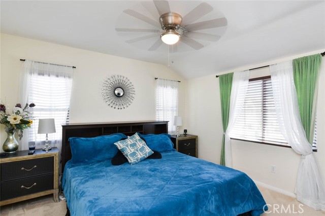 The light and bright master bedroom with ceiling fan and carpeted floor.