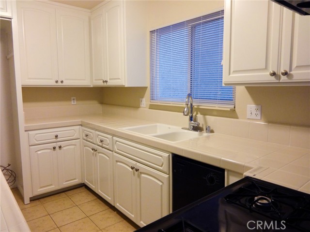 An older photo of the kitchen after renovation showing the sink, tile counters dishwasher and cabinets.