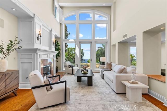 Living room with high ceiling and two-story windows, overlooking lush garden and the Pacific Ocean.