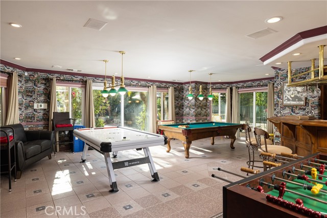  An expansive game room features a pub-style bar, private bathroom, billiards table and games, and direct access to the inviting pool area.