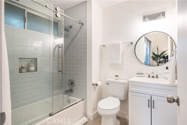 Remodeled, en suite primary bathroom with glass subway tiles and  glass barn door style enclosure.