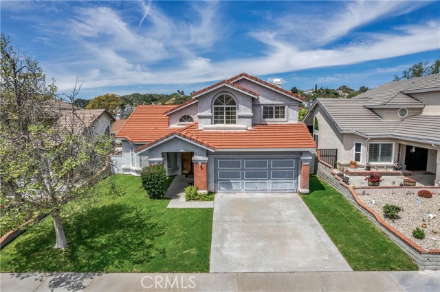 Well-situated in the highly desirable Copper Hill area is an appealing 2-story, 4 bed, 3 bath Mountain View home at 28809 Seco Canyon Rd. Boasting a spacious 2,214 sq ft layout on a generous 5,010 sq ft lot, this residence exudes warmth and comfort. Great curb appeal with a verdant lawn and striking herringbone-patterned brick columns welcoming you home. Step inside the double-door entry into a tiled entryway leading to an open-plan living and dining area offering soaring, 2-story, vaulted ceilings accentuated by wood beams. The large kitchen has great potential, featuring a central, butcher block island, tile counters, built-in gas range, electric oven, and room for a sunny breakfast nook. Adjacent is a cozy family room with a beautiful brick fireplace, perfect for gatherings, and sliding glass door access out to the back patio. The main floor also has a versatile bedroom with mirrored closets and an en-suite ¾ bath, ideal for guests or a home office. Upstairs, find a landing with built-in storage and three bedrooms.  Two sizable bedrooms offer mirrored closets and high ceilings, share a full hall bath with a double sink vanity. The primary bedroom is a private retreat with double door entry, high vaulted ceiling, bay window, spacious walk-in closet, and a full, en-suite bath with double sink vanity and dressing area. The large attached 2-car garage has direct access and ample storage space.  Additional features include a dedicated laundry area, newer AC, and newer furnace.  Outside, the pergola-covered patio and expansive lawn provide the perfect setting for relaxation or recreation in your own private domain. Enjoy the convenience of highly rated schools such as Mountainview Elementary and Academy of the Canyons, as well as proximity to shopping, dining, entertainment, and recreation options. With no HOA or Mello Roos, this is the epitome of comfortable, carefree living in the heart of Santa Clarita.