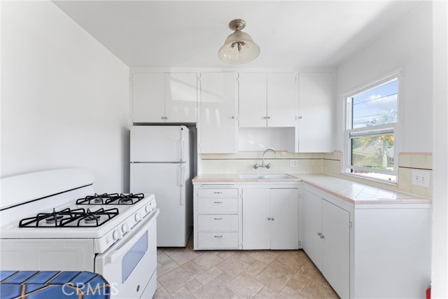 White and bright kitchen with tile counters, free standing oven and refrigerator. There is seperate access from kitchen to outside
