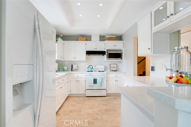 Upgraded Kitchen boasting of pristine white cabinets, quartz counter tops, a backsplash wall of glass mosaic tiles, an elegant ceiling with recessed lights, furnished with Refrigerator, Dishwasher and Gas Range & Stove.