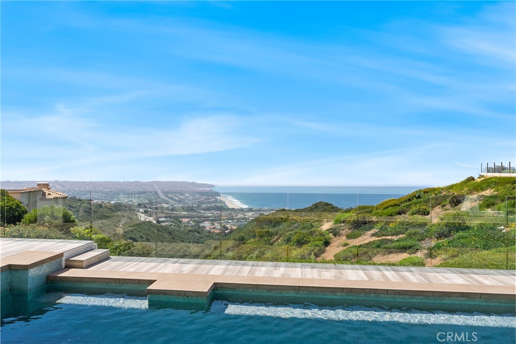 Set high above the coastline in the guard-gated enclave of Monarch Point, this newly transformed estate offers sweeping views from Dana Point’s cliffs to Monarch Bay’s coves. Every element of this hilltop retreat is curated for a refined lifestyle, blending indoor-outdoor living, modern style, and smart technology. A soaring 20-foot entry is crowned by a custom Murano glass chandelier. Floor-to-ceiling doors fill the home with light and open to a resort-style backyard with a pool, spa, porcelain deck, built-in DCS BBQ, and patio heaters—ideal for entertaining. The living room boasts a Napoleon linear fireplace framed in rare Black Carnelian stone, an 83” Sony Bravia TV, and five-speaker surround sound. A sleek bar with Sub-Zero fridges and Italian Cantoni cabinetry flows to a dining area with sunset views and a crystal chandelier. The chef’s kitchen features Thermador appliances, a Calacatta porcelain island, Fisher Paykel dishwashers, and a walk-in pantry. A breakfast nook sits beneath a glass chandelier and a frescoed ceiling by acclaimed artist Donovan Fitzgerald. The main level includes a private guest suite with separate entrance, kitchenette, full bath, and a Fitzgerald-painted ceiling. A dedicated office with LED lighting and custom shelving adds functionality. Upstairs, stainless double doors open to an ocean-facing primary suite with dual spa-like baths, walk-in closets, lounge with Napoleon fireplace and 83” Sony TV, and a full secondary kitchen. A Coverglass system opens to a wraparound balcony with panoramic views, fireplace, and another Fitzgerald fresco. Upgrades include new landscaping, pool/spa equipment with Aqualink, a 1,200-bottle wine cellar, tankless water heater, HVAC with Ecobee thermostats, Clare security with six Luma cameras, private elevator, Toto toilets, steam showers, and porcelain plank tiles throughout. Reverse osmosis systems serve all kitchens and bar sinks. A glass-floored landing under a skylight adds a striking architectural touch. Control4 automation and Lutron shades complete this smart coastal sanctuary. See Supplemental attachment for all the incredible details of upgrades!