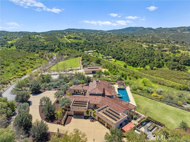 Unwind in LUXURY at this 28+ acre La Cresta Ranch Estate. This sought-after ranch offers breathtaking, panoramic unobstructed mountain views with complete privacy. Horse enthusiasts will find paradise with an upper pasture for grazing, a lighted riding ring, a very well-equipped barn featuring four stalls, automatic waterers, stall mats, a secure feed room, and a separate tack room with a half bath and 4-kennel dog run. This estate prioritizes sustainability with a recently installed brand new well and a meticulously maintained, upgraded irrigation system for water conservation. The seasonal retention basin replenishes groundwater, ensuring a responsible approach to water management. Access the property from two different entrances taking you through landscaped grounds and paved private roads. Step inside the exquisite 5-bedroom, 5 1/2-bathroom Ranch style estate including two separate exclusive suites with their own private entry access. Renovated with modern design elements throughout, wood beams ceilings, all new renovated master bathroom suite countertops with two water closets. The chef's kitchen boasts top-of-the-line appliances, stunning all-new high-end Taj Majal quartzite countertops, a Sub-Zero built-in refrigerator and a Wolf 6-burner range. Embrace seamless indoor/outdoor living with a California room, perfect for entertaining. The main bathroom features all-new countertops, dual sinks, and a central steam shower. The main suite boasts spacious dual walk-in closets, a fireplace and sliders leading directly out to the backyard, creating your own private oasis. Extend your sanctuary with a convenient outdoor bathroom featuring a shower and luxury amenities. Entertain in style with a sparkling 70"x20" saltwater pool, a 12'x20' spa, and a well-equipped outdoor bar and grill, two outdoor sinks, refrigerator, and ice maker. Discover a private family orchard featuring thriving avocados, various citrus fruits, stone fruits, and grapes. Stay connected with Starlink Wifi and enjoy with paid-off solar panels and a whole-house generator, with smart home wifi thermostats for convenience. Featuring a 5-car total garage in two spaces designed with new epoxy flooring, offering ample storage and a dedicated workspace both equipped with its own sink. A whole house stereo system and wifi throughout. This extraordinary property offers a unique and luxurious lifestyle, perfect for those seeking privacy, tranquility, and connection with nature.
