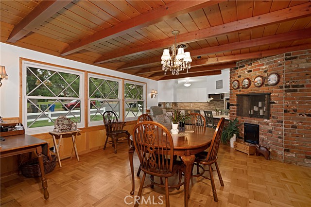 The spacious dining room features wood parquet flooring, open beam ceilings and a brick fireplace wall.