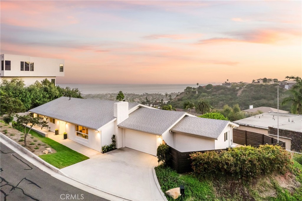 Situated on a private corner lot in the rolling hills of San Clemente, this meticulously maintained single-story home offers breathtaking panoramic ocean, city light, and sunset views. The home's charming curb appeal captivates from the moment you arrive, with a well-manicured front yard, sleek horizontal wood fence, and a refreshed modern look featuring a smooth stucco exterior and stylish lighting. Upgrades to the exterior concrete work enhance both the home's aesthetic and functionality. Expansive double-entry doors set the tone for a sophisticated interior, offering four bedrooms and two bathrooms with generous living space throughout. An open floor plan, bathed in natural light, showcases coastal vistas through large windows, wide-plank white oak engineered hardwood floors, crown molding, and a cozy gas fireplace with built-in accents. The kitchen reflects a coastal contemporary style, featuring top-of-the-line appliances, quartz countertops, modern flat-front cabinetry, peninsula seating, and pendant lighting. The primary suite is a serene retreat, with unobstructed sit-down ocean views providing a breathtaking backdrop and direct access to private outdoor living spaces. The ocean-view en-suite bath blends luxury and functionality, with a chic double vanity and spacious walk-in shower. Three additional bedrooms, a full bathroom, and a utility room with laundry area complete the interior, offering both comfort and versatility. The spacious backyard is an entertainer’s dream, featuring a large concrete patio and fresh landscaping—ideal for gatherings or soaking in stunning sunsets. With its prime location just minutes from scenic trails, downtown San Clemente, and the area's best beaches, this home offers the perfect blend of luxury, privacy, and coastal convenience.