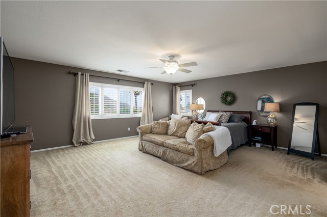 Primary bedroom with ceiling fan and window coverings.