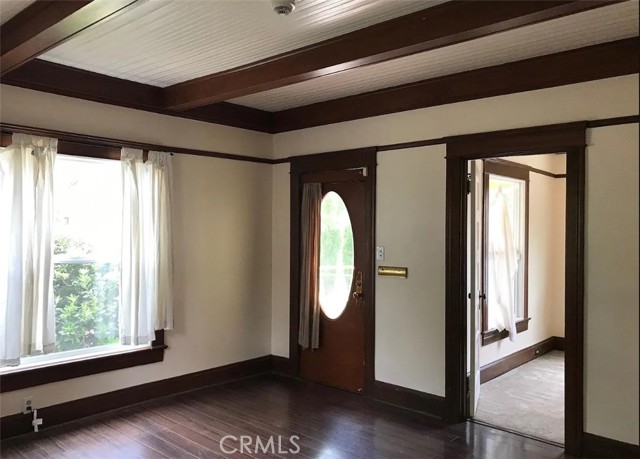 Living room with beamed ceilings, crown molding and hardwood floors.  Secondary bedroom through doorway on the right.