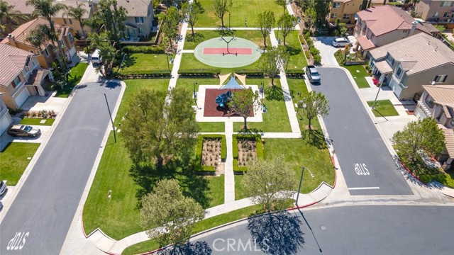 An aerial view of a community park with a basketball court and a playground, flanked by residential streets and houses with neatly landscaped yards. An aerial view of a community park with a basketball court and a playground, flanked by residential street