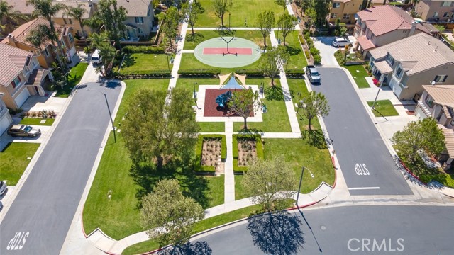 An aerial view of a community park with a basketball court and a playground, flanked by residential streets and houses with neatly landscaped yards. An aerial view of a community park with a basketball court and a playground, flanked by residential street