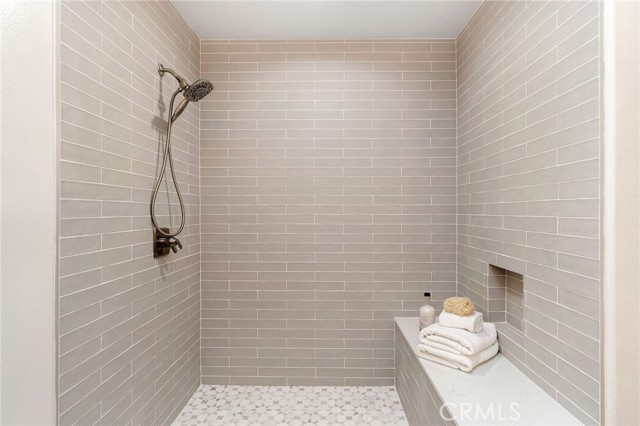 Neutral tones envelope this remodeled shower with quartz-flanked bench and luxurious white and grey veined stone floor.