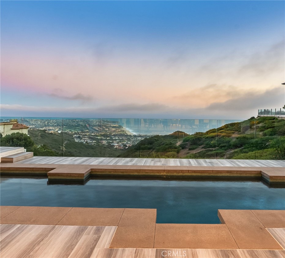 22842 Seaway Laguna Niguel, California Set high above the coastline in the guard-gated enclave of Monarch Point, this newly transformed estate offers sweeping views from Dana Point’s cliffs to Monarch Bay’s coves. Every element of this hilltop retreat is curated for a refined lifestyle, blending indoor-outdoor living, modern style, and smart technology. A soaring 20-foot entry is crowned by a custom Murano glass chandelier. Floor-to-ceiling doors fill the home with light and open to a resort-style backyard with a pool, spa, porcelain deck, built-in DCS BBQ, and patio heaters—ideal for entertaining. The living room boasts a Napoleon linear fireplace framed in rare Black Carnelian stone, an 83” Sony Bravia TV, and five-speaker surround sound. A sleek bar with Sub-Zero fridges and Italian Cantoni cabinetry flows to a dining area with sunset views and a crystal chandelier. The chef’s kitchen features Thermador appliances, a Calacatta porcelain island, Fisher Paykel dishwashers, and a walk-in pantry. A breakfast nook sits beneath a glass chandelier and a frescoed ceiling by acclaimed artist Donovan Fitzgerald. The main level includes a private guest suite with separate entrance, kitchenette, full bath, and a Fitzgerald-painted ceiling. A dedicated office with LED lighting and custom shelving adds functionality. Upstairs, stainless double doors open to an ocean-facing primary suite with dual spa-like baths, walk-in closets, lounge with Napoleon fireplace and 83” Sony TV, and a full secondary kitchen. A Coverglass system opens to a wraparound balcony with panoramic views, fireplace, and another Fitzgerald fresco. Upgrades include new landscaping, pool/spa equipment with Aqualink, a 1,200-bottle wine cellar, tankless water heater, HVAC with Ecobee thermostats, Clare security with six Luma cameras, private elevator, Toto toilets, steam showers, and porcelain plank tiles throughout. Reverse osmosis systems serve all kitchens and bar sinks. A glass-floored landing under a skylight adds a striking architectural touch. Control4 automation and Lutron shades complete this smart coastal sanctuary. See Supplemental attachment for all the incredible details of upgrades!