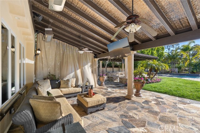 Outdoor living room with tin roof, heaters and fans, flagstone patio and a look toward the outdoor kitchen