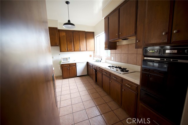 Kitchen has a 4 burner gas stove top, double oven with ceramic tile counters and tile flooring.