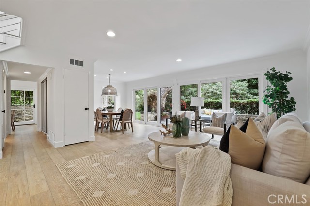 The expansive living room features a stone fireplace, complemented by built-ins, adjacent to a formal dining room – all seamlessly opening onto the wrap-around back patio, offering a side view of the Back Bay.