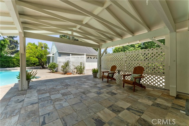 Covered patio with slate looking tile. Detached garage in distance with pool house adjacent.