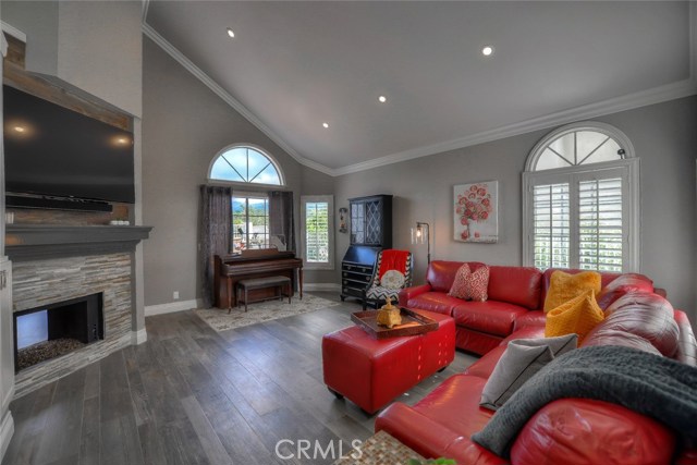 Living room with cathedral ceiling, recessed lighting, plantation shutters, gas fireplace, and wood-like tile flooring.