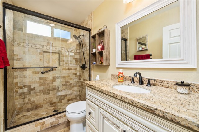 Remodeled bathroom with laminate floors, custom cabinetry with granite countertops, and a custom travertine tiled shower with a sliding glass enclosure.