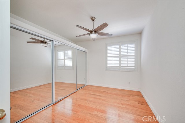 2nd bedroom with mirrored closet doors, plantation shutters and ceiling fan.