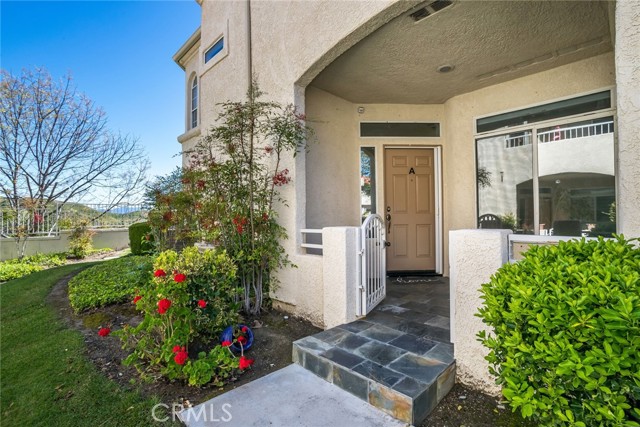 Welcome to this gated condominium, nestled at the top of Stevenson Ranch within the coveted Crown Villas neighborhood. Boasting 2 bedrooms and 2 baths, this adorable lower level home features nearly 1100 square feet of open living space. Upon entering enjoy inviting paint selections, oversized arched windows highlighting the views and new laminate wood flooring that extends a warm welcome throughout. The formal living room and dining area create an elegant ambiance, complemented by a cozy fireplace, perfect for gatherings or quiet evenings in. Step outside onto the gorgeous patio, a tranquil retreat where you can enjoy the beauty of the surrounding landscape. The kitchen features newer white appliances, granite counters, shaker cabinetry, all accented by a spacious breakfast bar with seating for three. The primary suite is a sanctuary of comfort with ample closet space, a private ensuite bath. and access to the patio with incredible views. Enjoy the convenience of an attached garage, additional carport, washer/dryer closet, and abundant storage options. Guests will appreciate the ample parking available within the community. Experience resort-style living with HOA amenities that include a sparkling pool, rejuvenating spa, and outdoor entertainment spaces. This home is surrounded by lush, grassy common areas, all against the backdrop of stunning mountain views. Situated near award-winning schools, shopping destinations, parks, and easy access to freeways. This home offers the epitome of comfortable and convenient living. Don't miss the opportunity to make this charming retreat your own.