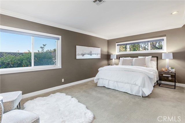 The primary bedroom is a spacious suite with designer color tones, crown moldings and baseboards, built-in cabinets and drawers, plush carpet, and recessed lighting.