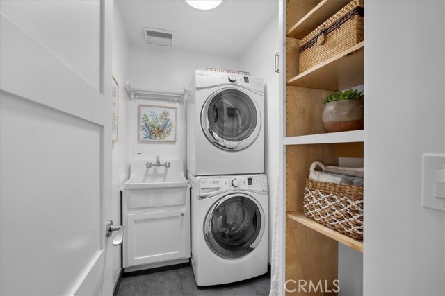 Dedicated laundry room with stack appliances and storage.