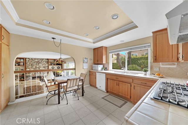 Large Country-Style Kitchen with Recessed Lighting, Tile Countertops, an Abundance of Natural Wood Cabinetry, and an Eat-In Breakfast Nook that Overlooks a Warm and Inviting Family