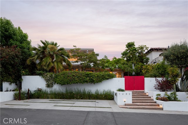Tucked behind privacy fencing on a quiet knoll, 1482 Carmelita Street in Laguna Beach offers a rare blend of privacy, flexible living space, and sweeping views. This thoughtfully designed 5-bedroom, 4-bathroom residence spans 2,200 square feet on a 4,550 square foot lot. Originally built in 2016, the property also includes a newly completed attached ADU (2025) with separate address, perfect for guests, rental income, or a dedicated office space. From nearly every corner of the property, enjoy vibrant garden views, dramatic mountain and city vistas, and even ocean peeks. The fully gated lot is surrounded by mature trees and lush landscaping, including fruit-bearing trees such as oranges, lemons, blueberries, blackberries, passion fruit, and grapes. Built with steel construction, the home is solid and enduring, with a master suite deck designed for optimal privacy and panoramic views. Inside, the home is flooded with natural light and features wood flooring, high-end appliances, custom finishes, and mini-split A/C and heating systems. The open layout seamlessly connects indoor and outdoor living spaces with Fleetwood sliders, cantina-style pass-through windows, a built-in BBQ, fire pit, wood-burning fireplace, and a striking custom entry door. Sustainability and modern convenience