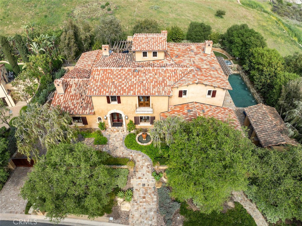This custom estate in Shady Canyon offers an exclusive retreat in one of Orange County’s most coveted enclaves. This 6 bedroom and 8 bath estate offers an elevator and includes two very rare and desirable features – two primary suites and an 8-car garage. Positioned on a private lot with no neighbor to one side, the residence spans three levels of refined luxury, blending architectural grandeur with modern comforts. The entryway leads to a dramatic foyer with a barrel-vaulted ceiling setting the stage for the formal dining room, adorned with intricate wood coffered ceilings and large windows. Adjacent is a spacious executive office, featuring built-in shelving, and also a formal sitting room with a cozy fireplace inviting intimate gatherings. The remodeled and airy chef’s kitchen showcases white marble countertops, extensive cabinetry for storage, and a large central island. High-end appliances are seamlessly integrated, and the butler’s kitchen provides functionality. The sun-filled breakfast room connects the kitchen and family room creating a warm space for everyday living and also opens effortlessly to the poolside terrace. The outdoor area is a true extension of the home where the refreshing pool beckons and the barbecue pavilion, lawn and putting green are complemented with stone elements and lush landscaping to create a setting shrouded in privacy. The main level includes a junior primary suite and guest suite, while the upper floor is home to two additional bedroom suites and the grand primary retreat. The primary bedroom suite offers a private kitchenette, stone fireplace, rich hardwood flooring, and opens to a spacious balcony through a wall of wooden framed glass doors, allowing natural light to fill the space while offering magnificent views of the surrounding hillside, mountain and city lights. The primary bath is an opulent haven with warm-toned marble, a walk-in shower, oversized dressing room and custom wood cabinetry. The subterranean level features a game room with coffered ceiling, a custom-built bar, gym with full bath, and a home theater outfitted with reclining seats, dark walls and sconces setting the ambiance for a true cinematic experience. For the true car enthusiast, this estate boasts an extraordinary 8-car garage that goes beyond mere parking. Designed with the collector in mind, the expansive space offers room for a prized fleet and is thoughtfully equipped with built-in cabinetry and workspace areas. This home is a must see!