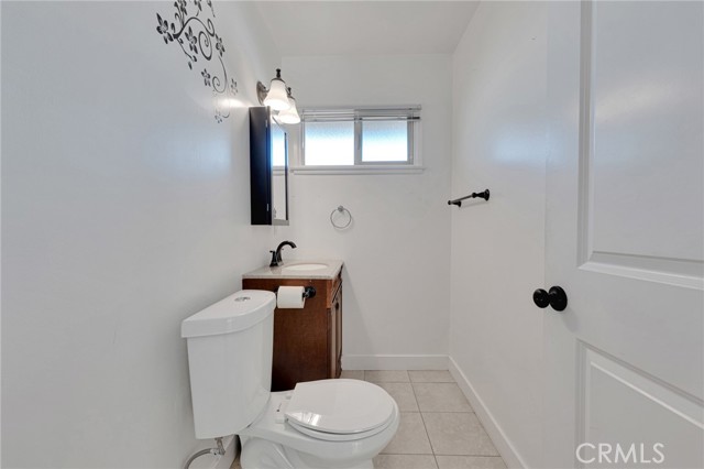 Powder room with single vanity, framed dressing mirror with sundry storage, designer lighting, single flush commode and tiled floors.