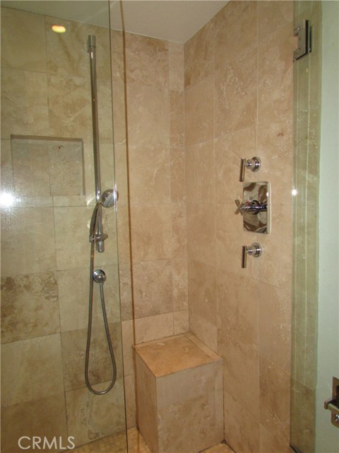 Custom stall shower with stone/travertine tile, quality chrome shower hardware with separate handheld spray handle and frameless shower enclosure.