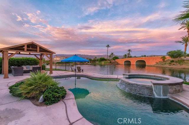 84350 Tramonto Way Indio, California Situated on a prime waterfront corner lot, this single-level residence is ideally positioned for enjoying the magnificent lake, bridge, and mountain views. Entertaining is easy here, with plenty of space to relax in the backyard, lounging by your own private pebble tec pool and spa with a waterfall, or sitting around the firepit. Indoors you'll love the open-concept living, dining and kitchen area; the chef's kitchen with its granite slab countertops, sizable island, and plenty of storage; the attractive wood-style flooring; the spacious and separated master retreat with walk-in closet, full bathroom, and even water views from the master bedroom. Ideal for an investment home that allows for short term rentals with profitable outcomes or a forever home for the family (This home has already been a successful STR with six figure income producing potential). Terra Lago is a guard gated community with low HOA dues and offers a man-made lake for electric boats and catch & release fishing. Terra Lago features a playground, community pool and spa, Clubhouse, fitness center and game room as well as a cable/internet service package.