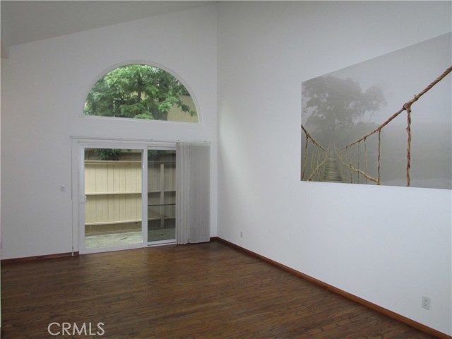 View of spacious living room from entry with true hardwood floors, vaulted ceiling and arched clerestory window with serene tree views and northern exposure.